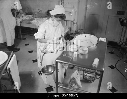 DAS HAUS WIRD ZUM ENTBINDUNGSHEIM: LIFE AT BROCKET HALL, WELWYN, HERTFORDSHIRE, 1942 - Eine Studentin bereitet ein Baby auf ein Bad in Brocket Hall vor. Die Krankenschwester trägt eine chirurgische Maske, um die Ausbreitung von Keimen auf das Baby zu verhindern Stockfoto