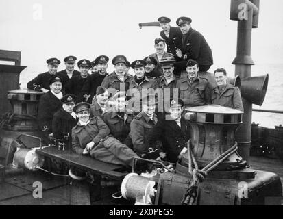 DAS LEBEN UND WERK EDWARD G MALINDINE, FOTOJOURNALIST UND OFFIZIELLER MILITÄRFOTOGRAF 1906–1970 an Bord der LSI HMS PRINCE LEOPOLD nach dem Combined Operations RAID auf Vaagso, Norwegen, 27. Dezember 1941. Der offizielle Fotograf des Kriegsministeriums, Lieutenant Edward G Malindine (Vordergrund) und andere Mitglieder der Pressepartei mit Mitgliedern der Schiffsbesatzung. Hinter Malindine sitzen von links nach rechts: Die offiziellen Kameramänner des Kriegsamtes Sgt Gerry Massy Collier und Lt Harry Rignold mit dem zivilen Kameramann Jack Ramsden von Movietone News Stockfoto