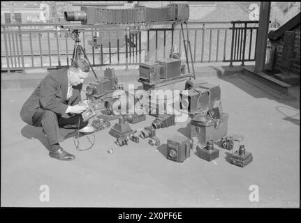 THE MAKINGS OF A MODERN NEWSPAPER: THE DAILY MAIL IN WARTIME, LONDON, UK, 1944 – der Fotograf Frank Rust von Daily Mail zeigt einige der Kameras, die er für seine Arbeit verwendet. Sie reichen von einer 35-mm-Contax bis hin zu einer speziell entwickelten Kamera mit 60-Zoll-Teleobjektiv Stockfoto