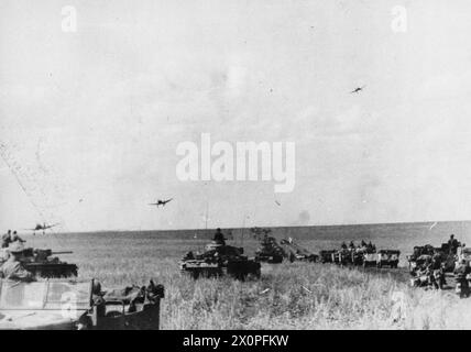 Junkers Ju 87 Stuka-Tauchbomber fliegen in der Schlacht bei Kursk im Juli 1943 tief über vorrückende deutsche Panzer III-Panzer und Softskin-Fahrzeuge an der Orel-Front. Stockfoto