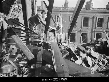 LONDON ZEIGT DIE FLAGGE: LIFE GOES ON WARTIME LONDON, ENGLAND, 1940 – Ein kleiner Junge namens Leslie pflanzt eine Union Flag in den Schutt und Trümmer, der nach einem Luftangriff auf London 1940 von seinem Haus übrig ist Stockfoto