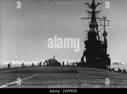 AN BORD DES BRITISCHEN LEICHTFLOTTENTRÄGERS HMS VENERABLE. JUNI 1945, AKTIVITÄTEN AN BORD DES EHRWÜRDIGEN FLAGGSCHIFFS DER 11. FLUGZEUGTRÄGER-STAFFEL. - Szene vom Ende des Flugdecks, in der EHRWÜRDIGE über die Absperrdrähte blickten, die einen luftverlegten Rauchschirm zeigen, kurz nachdem er fertig war. Auf dem Deck wird ein Fairey Barracuda mit gefalteten Flügeln von der Flugzeugabfertigung in Richtung der hinter dem Aufzug liegenden Wand bewegt (im Vordergrund offen gesehen). Stockfoto