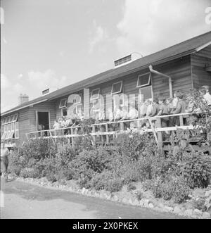 SCHULE FÜR EVAKUIERTE: ALLTAG IN MARCHANT'S HILL CAMP SCHOOL, HINDHEAD, SURREY, ENGLAND, GROSSBRITANNIEN, 1944 - Kinder stehen vor der großen Holzhütte, die als Speisesaal der Marchant's Hill School in Hindhead dient, in der Sonne zum Mittagessen an Stockfoto