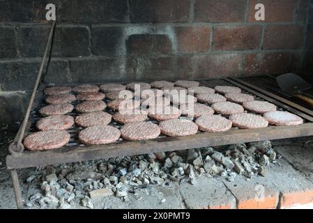 Ein Grill voller Hamburger kocht auf einem Backofen. Die Burger haben alle verschiedene Größen und werden auf einem Metallgitter gekocht. Die Szene hat einen Rost Stockfoto