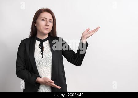 Kaukasische Frau, die mit dem Finger auf die Seite des Produkts zeigt oder einen leeren Kopierraum auf weißem Hintergrund. Ernste Erwachsene Geschäftsfrau mittleren Alters Stockfoto