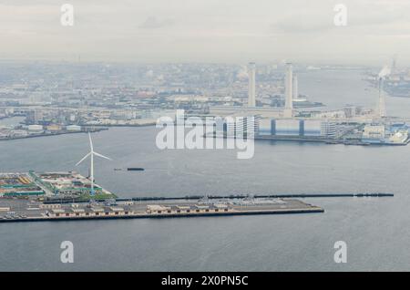 Der Aussichtspunkt aus der Luft bietet einen weiten Blick auf ein Industriegebiet von Port Citys und zeigt eine weiße Windturbine, die sich von der Cluster abhebt Stockfoto