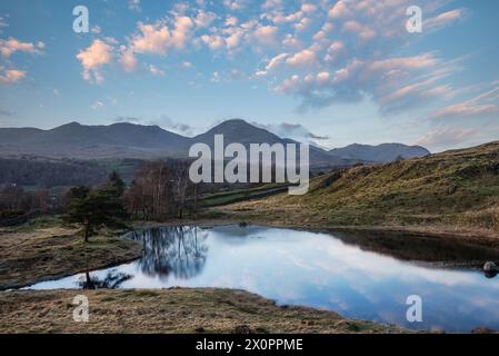Wunderschönes Bild der Sonnenuntergangslandschaft von Kelly Hall Tarn im Lake District mit Old man of Coniston im Hintergrund Stockfoto