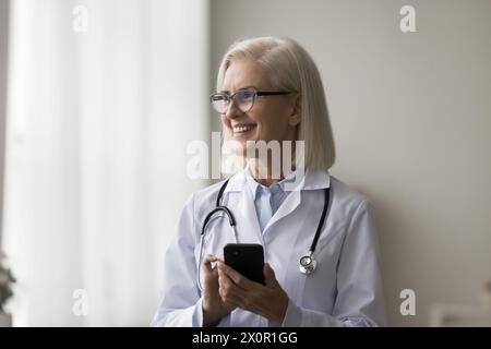 Reife Ärztin am Arbeitsplatz mit Smartphone Stockfoto
