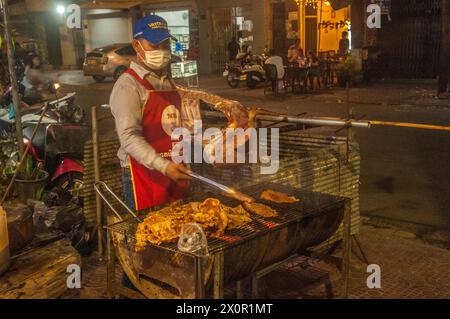 Während des kambodschanischen Neujahrsfestes grillt ein maskierter Khmer-Mann Fleisch in einem Open-Air-BBQ-Restaurant. Phnom Penh, Kambodscha. April 2024. © Kraig Lieb Stockfoto