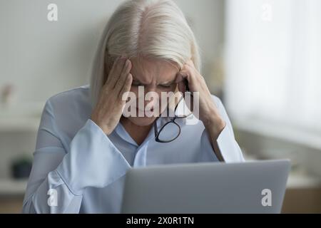 Frau, die neben Laptop sitzt, Brille abnimmt, leidet an Migräne Stockfoto