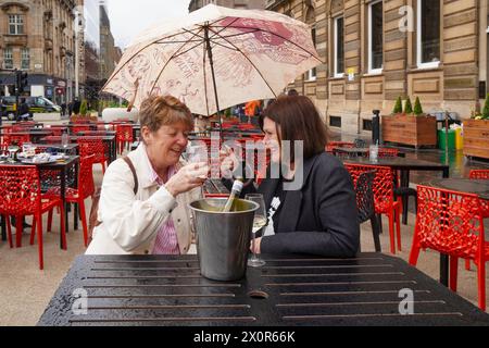 Glasgow, Großbritannien. April 2024. Leyanne und Wendy, die Glasgow von Edinburgh aus besuchen, lassen sich von dem schlechten Wetter und dem starken Regen nicht abschrecken und genießen ein Glas Wein im Freien im George Square, Glasgow, Schottland, UK Credit: Findlay/Alamy Live News Stockfoto