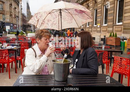 Glasgow, Großbritannien. April 2024. Leyanne und Wendy, die Glasgow von Edinburgh aus besuchen, lassen sich von dem schlechten Wetter und dem starken Regen nicht abschrecken und genießen ein Glas Wein im Freien im George Square, Glasgow, Schottland, UK Credit: Findlay/Alamy Live News Stockfoto