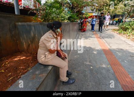 Eine Polizistin sitzt an einer Wand und telefoniert mit ihrem Handy in Bangalore, Bengaluru, Karnataka, Indien Stockfoto