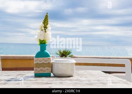 Lagerhaus im Freien. Stühle und Tische draußen bei Sommersonnenwetter. Vase mit Blumen auf dem Tisch für ein Sommercafé mit Meerblick. Stockfoto