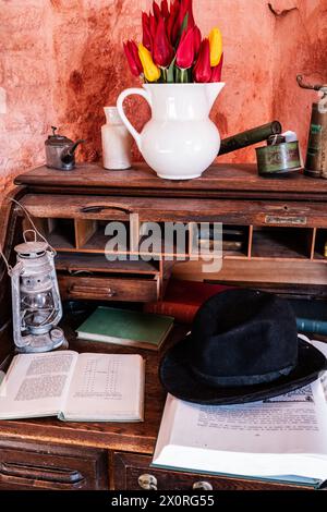 Eine antike Hurrikanlampe, Bowler Hut, weiße Vase, französische Tabakdose, offene Bücher und Messingspritzen auf einem altmodischen Holzbüro. Retro-Style. Stockfoto