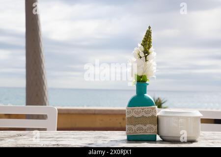 Lagerhaus im Freien. Stühle und Tische draußen bei Sommersonnenwetter. Vase mit Blumen auf dem Tisch für ein Sommercafé mit Meerblick. Stockfoto