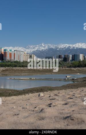 Speicherreservoir Sayran-See, Almaty, Kasachstan. Leerer City Sandstrand mit entwässertem Teich. Wohnhäuser und hohe schneebedeckte Montage Stockfoto