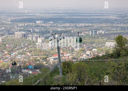 Seilbahn mit zwei Kabinen, vor dem Hintergrund der Stadt im Frühling. Mit dem Flugzeug zum Kok Tobe Hügel in Almaty, Kasachstan. Touristenort, City la Stockfoto