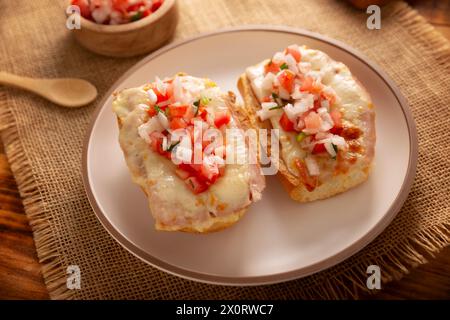 Molleten. Mexikanisches Rezept basierend auf Bolillo-Brot, das längs geteilt wird, mit gebratenen Bohnen und Gratin-Käse bestrichen wird, mit Pico de gallo-Sauce und etwas Pro Stockfoto