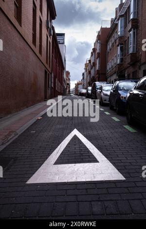 Urbane Szene. Ein „Ertrag“-Schild hebt sich vor dem schwarzen Asphaltgrund der Stadt ab, geparkte Autos, urbane Mobilität, Respekt, Verkehr, und Sonnenaufgang im Th Stockfoto