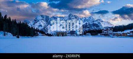 Panoramablick auf den gefrorenen und schneebedeckten See Lago di Misurina mit der Berggruppe Punta Sorapiss in der Ferne im Winter bei Sonnenuntergang. Misuri Stockfoto