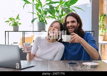 Glückliches lachendes junges Paar, das zusammen in der Cafeteria auf den Laptop blickt Stockfoto