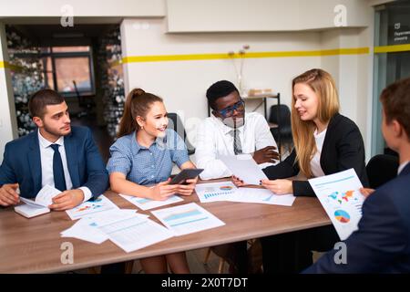 Multiethnische Geschäftsteams arbeiten am Bürotisch zusammen. Asiatische, afrikanische, kaukasische, arabische Kollegen diskutieren, Diagramme analysieren, planen Stockfoto