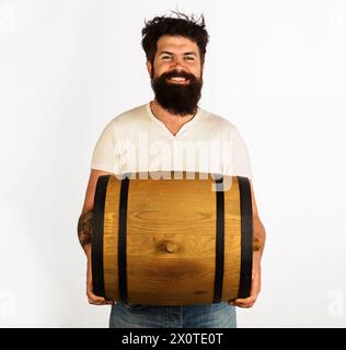 Lächelnder bärtiger Mann mit Fass oder Fass Whiskey, Wein oder Bier. Schöner Mann mit Eichenfässern oder Bierfässern. Bier für Pub oder Bar. Brühmaschine mitführen Stockfoto