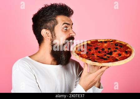 Pizza Zeit. Schöner bärtiger Mann mit leckerer Pizza. Mittag- oder Abendessen. Zufriedener hungriger Mann in Freizeitkleidung, der leckere Pizza genießt. Italienische Küche Stockfoto