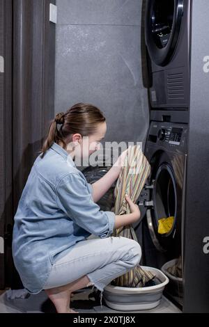 Die junge Frau nimmt die gewaschenen Kleider zu Hause aus der Waschmaschine. Stockfoto