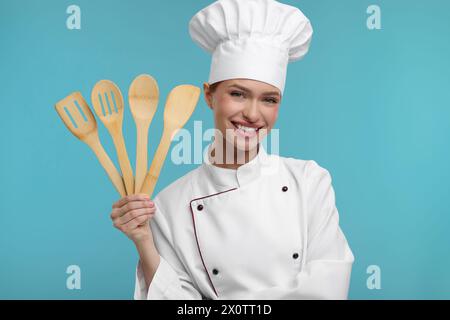 Glücklicher Koch in Uniform, der Holzutensilien auf hellblauem Hintergrund hält Stockfoto