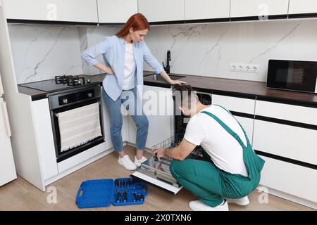 Frau, die sieht, wie ein Soldat ihren Geschirrspüler in der Küche repariert Stockfoto