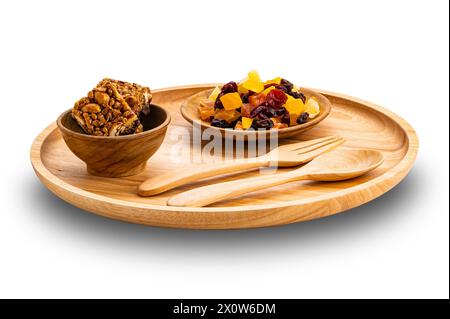 Ansicht von Proteinstäben in Holzschüssel mit gemischten getrockneten tropischen Früchten in Holzschale und Holzfrosch und Löffel in Platte isoliert auf weißem Hintergrund wi Stockfoto