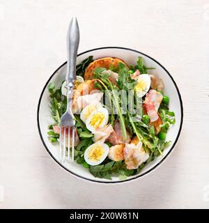 Frischer Sommersalat aus Löwenzahnblättern, Eiern, Speck und mit Brot auf hellem Hintergrund. Draufsicht Stockfoto
