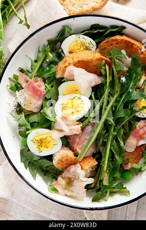 Frischer Sommersalat aus Löwenzahnblättern, Eiern, Speck und mit Brot auf hellem Hintergrund. Draufsicht Stockfoto