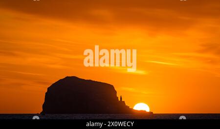 Firth of Forth, Schottland, Großbritannien, 14. April 2024. Wetter in Großbritannien: Sonnenaufgang über dem Bass Rock. Zu dieser Jahreszeit ist es möglich, einen Blick auf den Sonnenaufgang hinter der Tölpellerkolonie von der Ostlothianischen Küste vor einem leuchtenden orangen Himmel zu werfen. Quelle: Sally Anderson/Alamy Live News Stockfoto