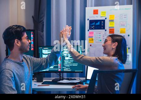 asiatische und indische Entwicklerteams klatschen sich für Projekterfolg mit Software-Computer in der Nacht im Büro Stockfoto