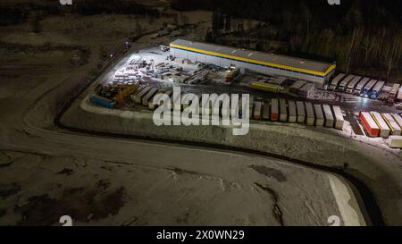 Drohnenfotografie von Logistiklagern und geparkten LKWs während der winterlichen bewölkten Nacht Stockfoto