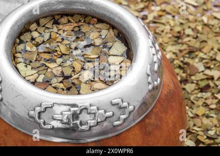 Mate Tee in einer typischen südamerikanischen Kalabash, mit getrockneten Blättern daneben Stockfoto