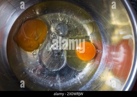 Zwei Eier stehen in einer Metallschale mit Öl in einer Metallrührschüssel und können in ein köstliches Gericht eingearbeitet werden. Die kontrastierenden Farben der Eigelbe und Stockfoto