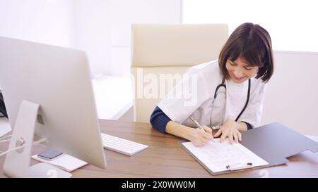 Doktor, der einen medizinischen Bericht ausfüllt, sitzt auf dem Schreibtisch Stockfoto