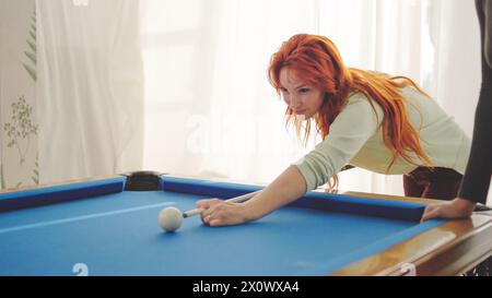 Konzentrierte Frau, die einen Billardball trifft, spielt mit Freunden Stockfoto
