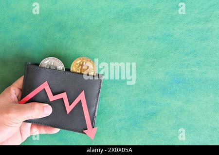 Menschliche Hand, die schwarz eine Brieftasche mit Bitcoin hält und unten roten Pfeil und Münze innen. Kryptowährungen, Bärenlauf und Preissenkungskonzept. Stockfoto