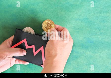 Menschliche Hand, die schwarz eine Brieftasche mit Bitcoin hält und unten roten Pfeil und Münze innen. Kryptowährungen, Bärenlauf und Preissenkungskonzept. Stockfoto