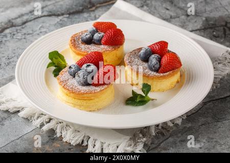 Japanische weiche Pfannkuchen mit Erdbeeren und Heidelbeeren, bestreut mit Puderzucker, Nahaufnahme auf einem Teller auf dem Tisch. Horizontal Stockfoto