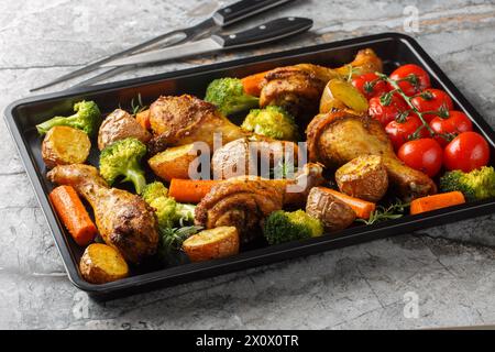 Im Ofen gebackene Hähnchenkeulen mit frisch gebackenem Gemüse in Nahaufnahme auf einem Backblech auf dem Tisch. Horizontal Stockfoto