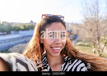 Porträt einer Latina-Frau, die ein Selfie mit ihrem Smartphone macht, während sie ein lustiges Gesicht macht und ihre Zunge herauszieht. Stockfoto