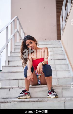 Junge Latina, die auf der Treppe sitzt und auf die Kamera blickt Stockfoto