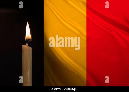 Trauerkerze brennt vor der belgischen Flagge, Erinnerung an Helden, die dem Land dienten, Trauer über den Verlust, nationale Einheit in schwierigen Zeiten, Geschichte des Staates Stockfoto