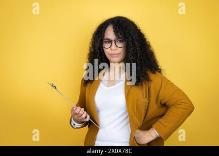 afroamerikanische Geschäftsfrau mit Papierkram in den Händen auf gelbem Hintergrund skeptisch und nervös, missbilligend Ausdruck auf Gesicht mit Armen in der Taille Stockfoto